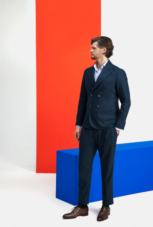 Daniel Hiemer, Partner Tax bei Kirkland & Ellis in München, stehend im blauem Anzug vor Hintergrund mit orangefarbenem vertikalen Streifen und blauer Box am Boden